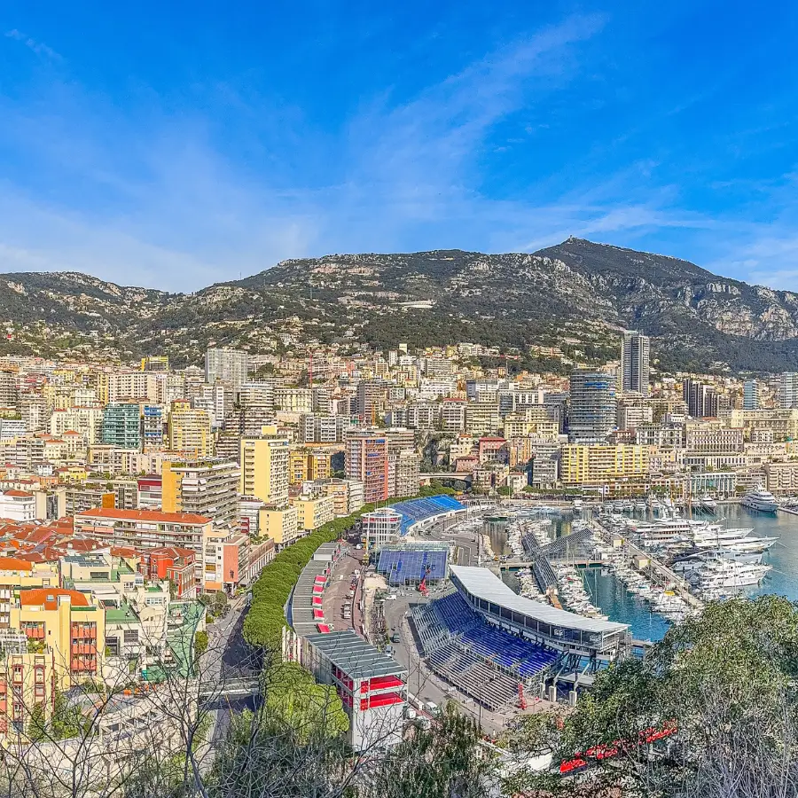 anoramic view of Monaco featuring the Formula 1 street circuit, marina, city buildings and surrounding mountains.