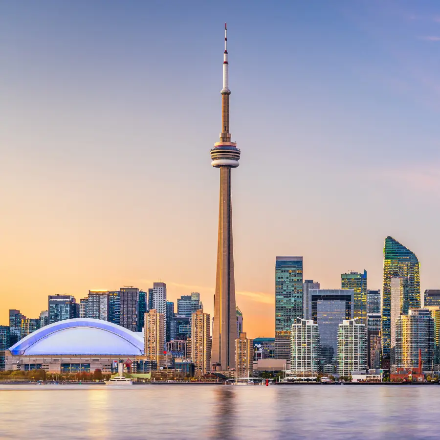 CN Tower rising above the Toronto skyline at sunset, with the Rogers Centre and waterfront in the foreground.