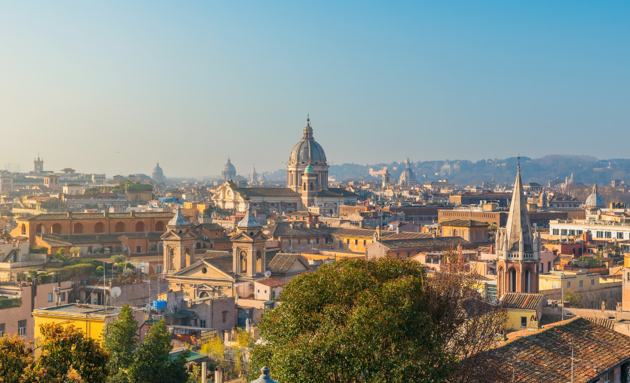 Panoramic view of Rome, Italy, featuring historic domes, church towers and terracotta rooftops under a clear blue sky.