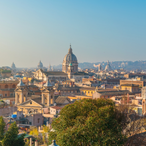 Panoramic view of Rome, Italy, featuring historic domes, church towers and terracotta rooftops under a clear blue sky.