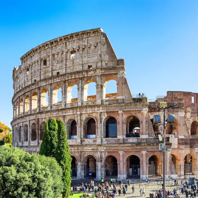 Exterior view of the Colosseum in Rome, Italy, with its historic stone arches beneath a bright blue sky.
